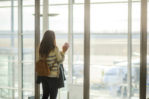 A woman with a backpack standing at the large window in the airport.