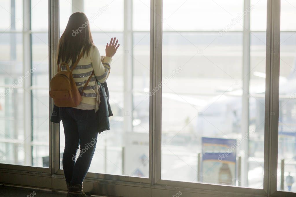 A woman with a backpack standing at the large window in the airport.