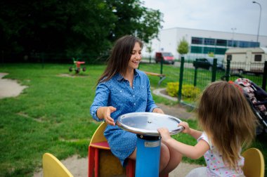 Genç anne oyun alanında küçük kızı ile oynuyor..