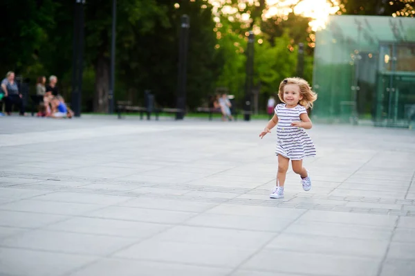 Söt liten flicka kör runt torget i en stadspark. — Stockfoto