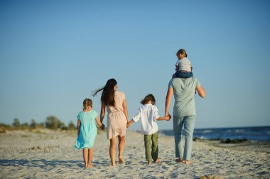 Big happy family walking at the beach. Mom, dad and three children. The blue sky, the sun, fresh sea wind. Pleasure from nature and communication. clipart