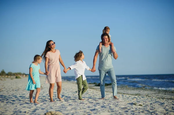 Большая счастливая семья, гуляющая по пляжу. Мама, папа и трое детей. Голубое небо, солнце, свежий морской ветер. Удовольствие от природы и общения . — стоковое фото