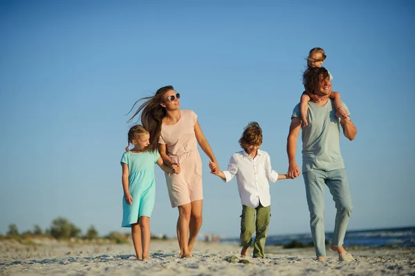 Μεγάλη ευτυχισμένη οικογένεια που περπατούν στην παραλία. Μαμά, μπαμπάς και τρία παιδιά. Το γαλάζιο του ουρανού, τον ήλιο, θαλασσινό αέρα. Ευχαρίστηση από τη φύση και την επικοινωνία. — Φωτογραφία Αρχείου