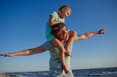 Genç adam şen şakrak denizin kenarında küçük kızıyla vakit geçiriyor.