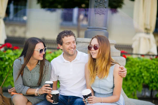 Twee meisjes en een jongen zijn koffie drinken en praten levendige. — Stockfoto