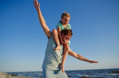 Genç adam şen şakrak denizin kenarında küçük kızıyla vakit geçiriyor.