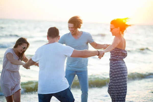 Groep van vrolijke jonge mensen dansen hebben toegetreden handen op het strand. — Stockfoto
