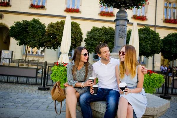 Två tjejer och en kille dricker kaffe och pratar livliga. — Stockfoto