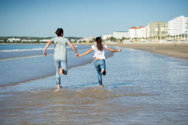 Man and woman running barefoot through the water. — Stock Photo, Image