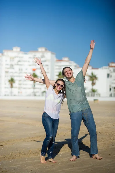 Cheerful young couple costs in wet clothes on the beach.