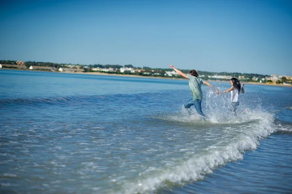 Het jonge paar loopt in de zee, het verhogen van spatten. — Stockfoto