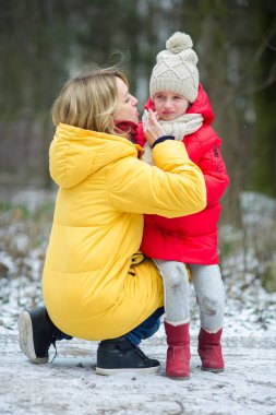 Young mother consoles the crying child. The girl has fallen during walk. For her it is sick and offensive. The loving mother calms the daughter. Against the background of the winter park. clipart