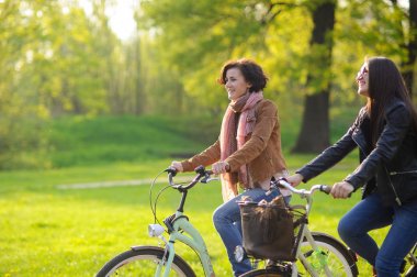İki genç çekici kadın bahar parkta bisiklet sürmek. Doğa ve hareketleri tarafından zevk. Sağlıklı yaşam tarzı.