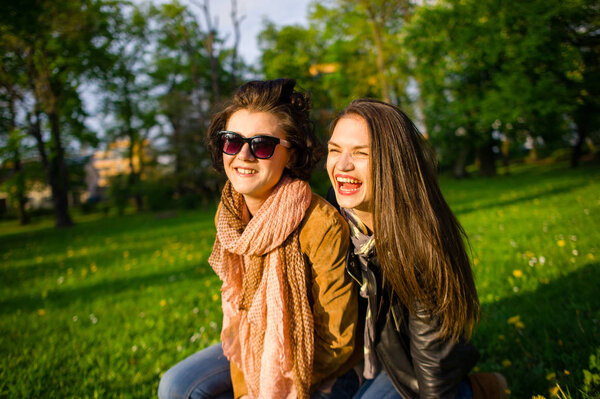 Two cute young women cheerfully spend time in the spring park. Women have a playful mood. Warm sunny day. Girlfriends enjoy the nature and communication.