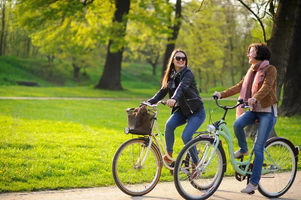 Two young attractive women ride bikes in the spring park. Pleasure by nature and movements. Healthy lifestyle.