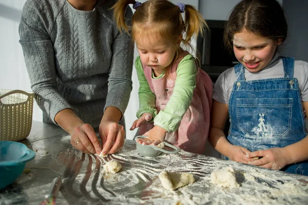 Maman enseigne à deux petites filles à cuisiner à partir de la pâte . — Photo