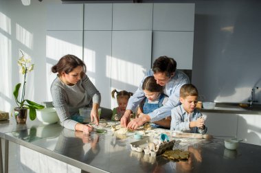 Geniş aile hamurdan bir şeyler hazırlar. Ebeveynler ve üç çocuk mutfak masasında. Mutlu ve kullanışlı eğlence.