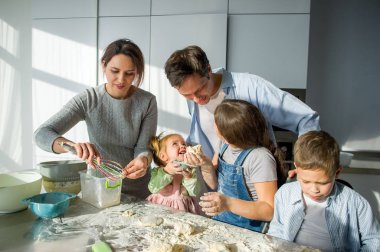 Geniş aile hamurdan bir şeyler hazırlar. Ebeveynler ve üç çocuk mutfak masasında. Mutlu ve kullanışlı eğlence.