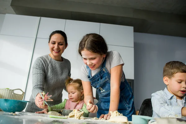 妈妈教她的三个孩子做饭 家人正在用面团准备一些东西 厨房桌子上有必要的产品 有益和有趣的消遣 — 图库照片