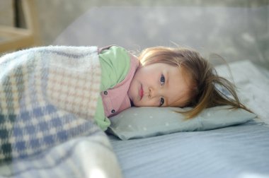 Little girl falls asleep on the bed. Baby is covered with a plaid. clipart