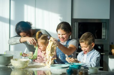 Anne üç çocuğuna yemek yapmayı öğretiyor. Aile hamurdan bir şeyler hazırlıyor. Mutfak masasında gerekli ürünler var. Faydalı ve eğlenceli bir eğlence..