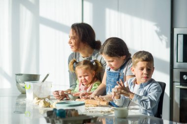 Anne üç çocuğuna yemek yapmayı öğretiyor. Aile hamurdan bir şeyler hazırlıyor. Mutfak masasında gerekli ürünler var. Faydalı ve eğlenceli bir eğlence..
