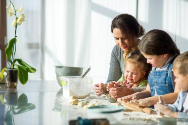 Anne üç çocuğuna yemek yapmayı öğretiyor. Aile hamurdan bir şeyler hazırlıyor. Mutfak masasında gerekli ürünler var. Faydalı ve eğlenceli bir eğlence..
