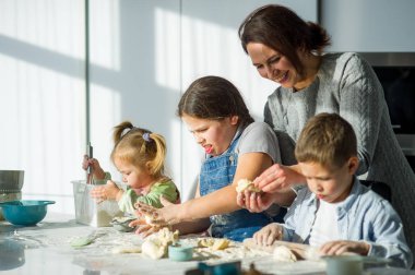Anne üç çocuğuna yemek yapmayı öğretiyor. Aile hamurdan bir şeyler hazırlıyor. Mutfak masasında gerekli ürünler var. Faydalı ve eğlenceli bir eğlence..