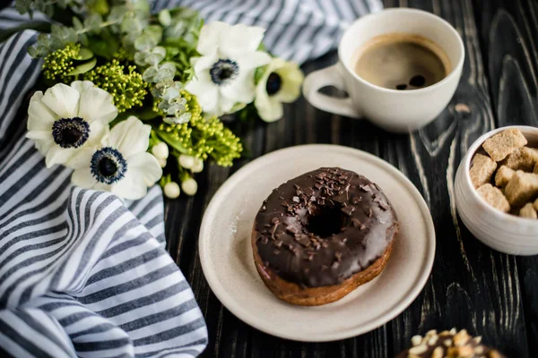 Xícara de café e um donuts de chocolate em madeira preta — Fotografia de Stock