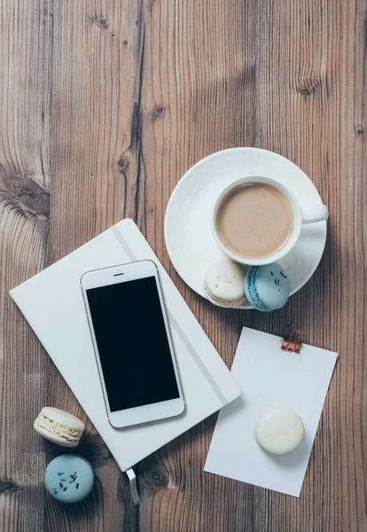 Чашка кави, сині макаруни та смартфон на дерев'яному столі — стокове фото
