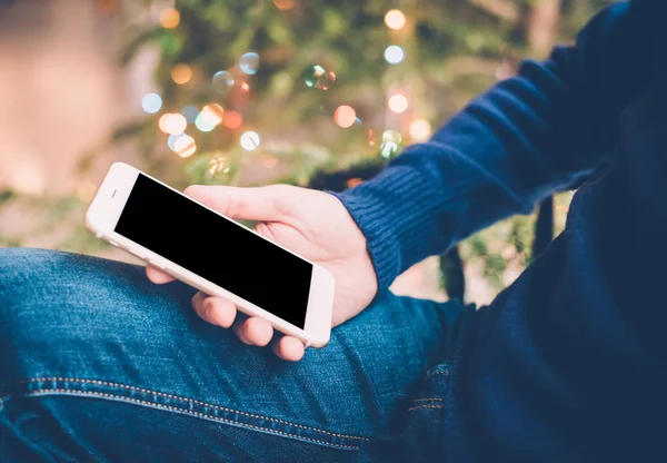 Hombre relajante en casa con teléfono inteligente en la mano, vacaciones acogedoras e — Foto de Stock