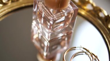 Golden earrings with gemstones and perfume on mirror tray