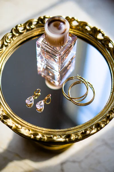 Złote kolczyki z kamieniami szlachetnymi i perfumami na tacy lustrzanej — Zdjęcie stockowe