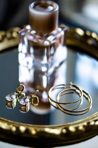 Golden earrings with gemstones and perfume on mirror tray — 图库照片