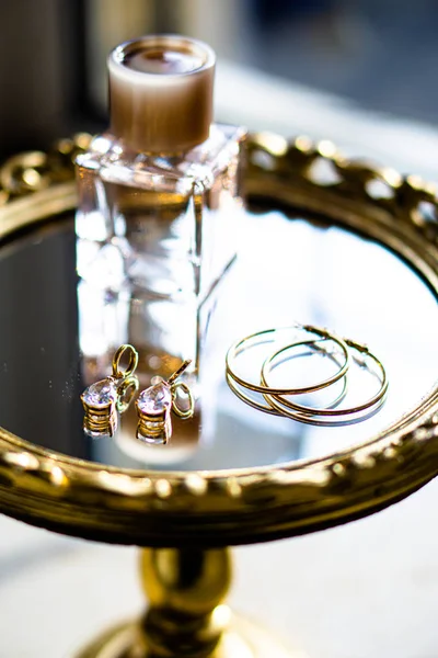 Golden earrings with gemstones and perfume on mirror tray — 图库照片