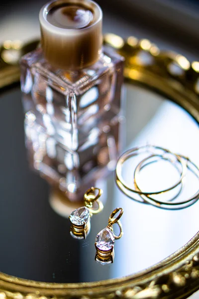 Złote kolczyki z kamieniami szlachetnymi i perfumami na tacy lustrzanej — Zdjęcie stockowe