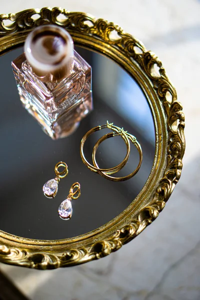 Golden earrings with gemstones and perfume on mirror tray — 图库照片