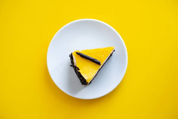 노란색 배경에 주황 젤리가 달린 초콜릿 케이크 조각 — 스톡 사진