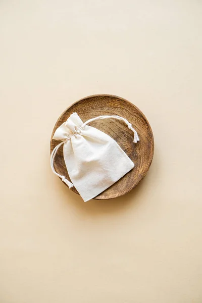 Small linen bag in wooden plate on beige background — Stock Photo, Image