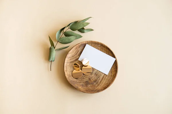 Naturzweig mit Blättern und goldenen Ohrringen in Holzteller auf beigem Hintergrund — Stockfoto