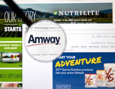 MONTREAL, CANADA - MARCH 10, 2018: Amway web page under magnifying glass. Amway is an American company specializing in the use of multi-level marketing to sell health, beauty, and home care products. clipart