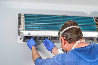 Mavi eldivenli ve maskeli teknisyen klimayı söküp temizlemeye hazırlıyor. Klima temizlemek, insanlar için tehlikeli olabilecek küflerin büyümesini önler..