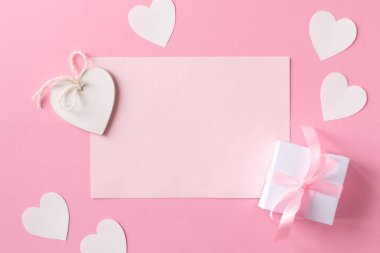 Kurdeleli hediye, beyaz tahta kalpler, pembe kağıt ve pembe arka planda kağıt kalpler. Düz yerde, üst tarafta. Sevgililer Günü konsepti.