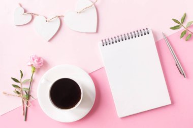 Temiz sayfalı defter, bir fincan kahve, çiçek, kalem ve pembe arka planda tahta kalp. Üst görünüm, düz görünüm.