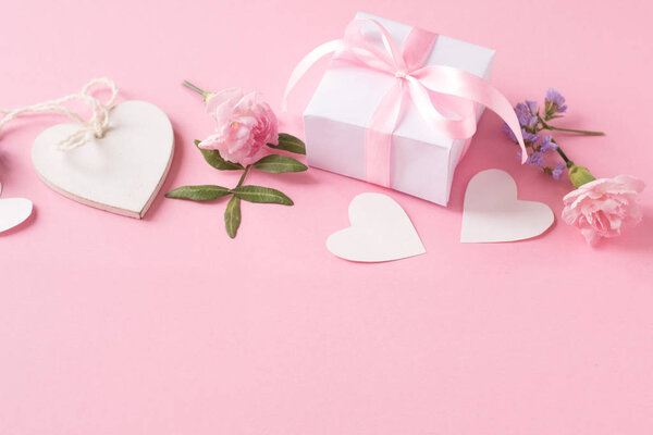Gift, wooden white heart and flowers on pink background