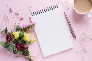 Çiçek buketi, defter, pembe arka planda kalem ve kahve.