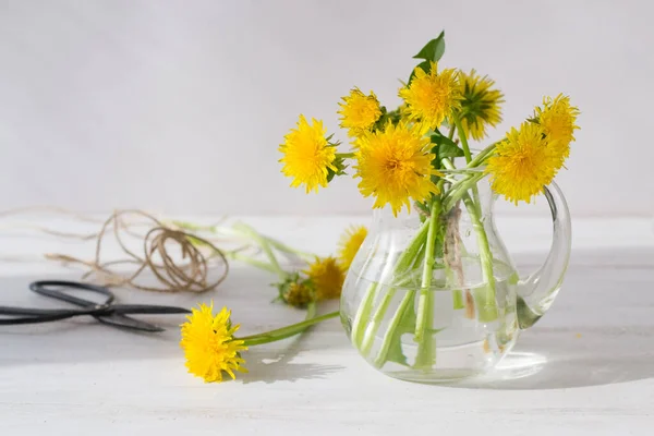 A bouquet of dandelions in white vase on a white wooden background, with copy space