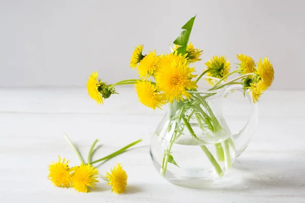 A bouquet of dandelions in white vase on a white wooden background, with copy space