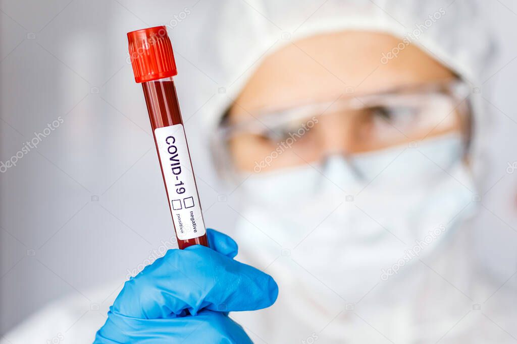 Covid 19 Coronavirus infected blood in tube in hand of scientist female doctor biohazard protection clothing in coronavirus research laboratory. Coronavirus Covid-19 vaccine research