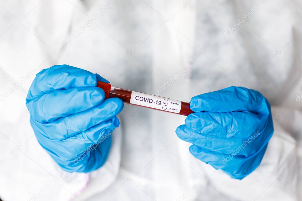 Covid 19 Coronavirus infected blood in tube in hand of scientist doctor biohazard protection clothing in coronavirus research laboratory. Coronavirus Covid-19 vaccine research.